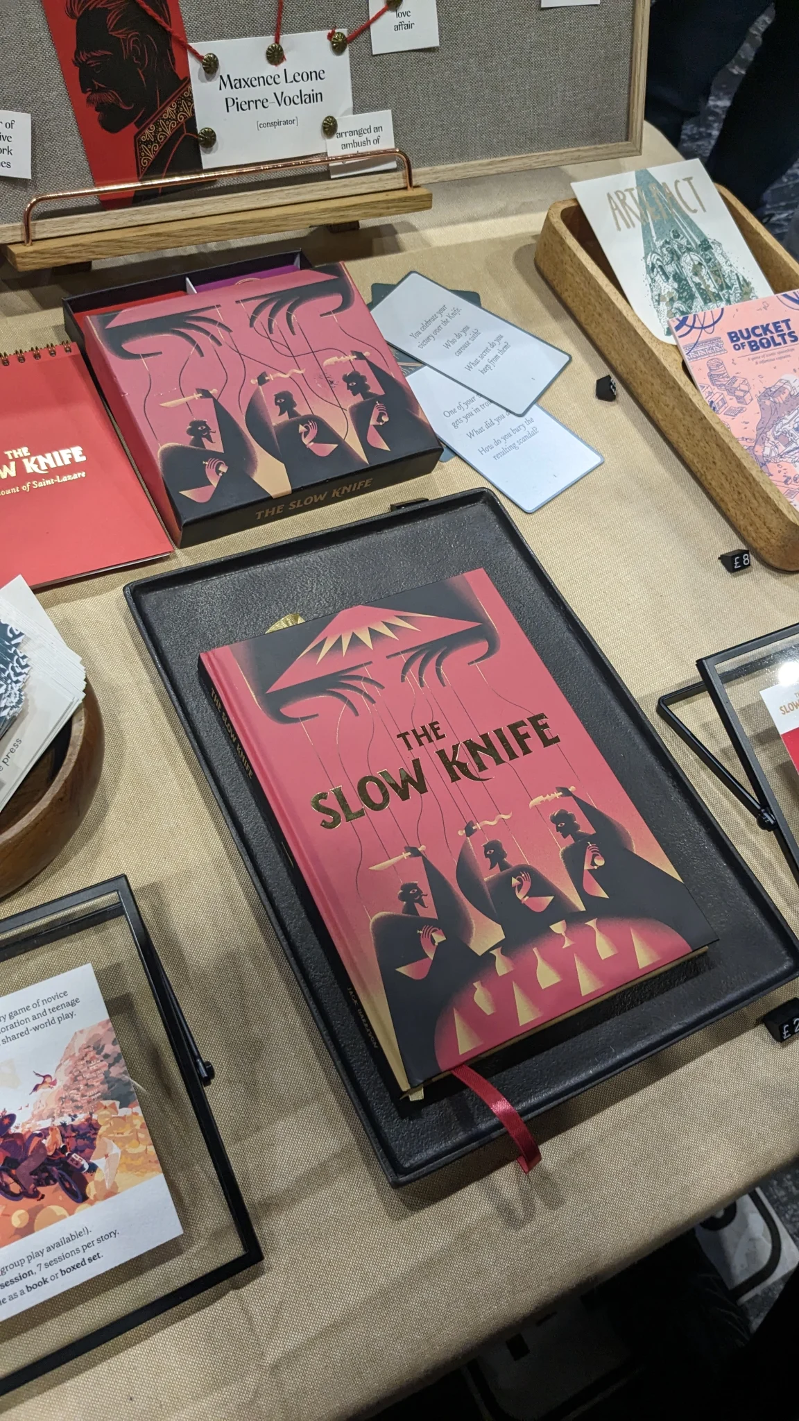 The slow knife RPG book with the previous edition of the game, with cards, above it.